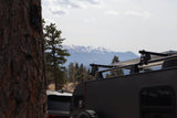 An RV rental teardrop trailer with solar panels, set against snow-capped mountains and a forest, hinting at outdoor adventures.