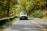 RV rental van on a scenic autumn road, surrounded by vibrant fall foliage and a stone wall.