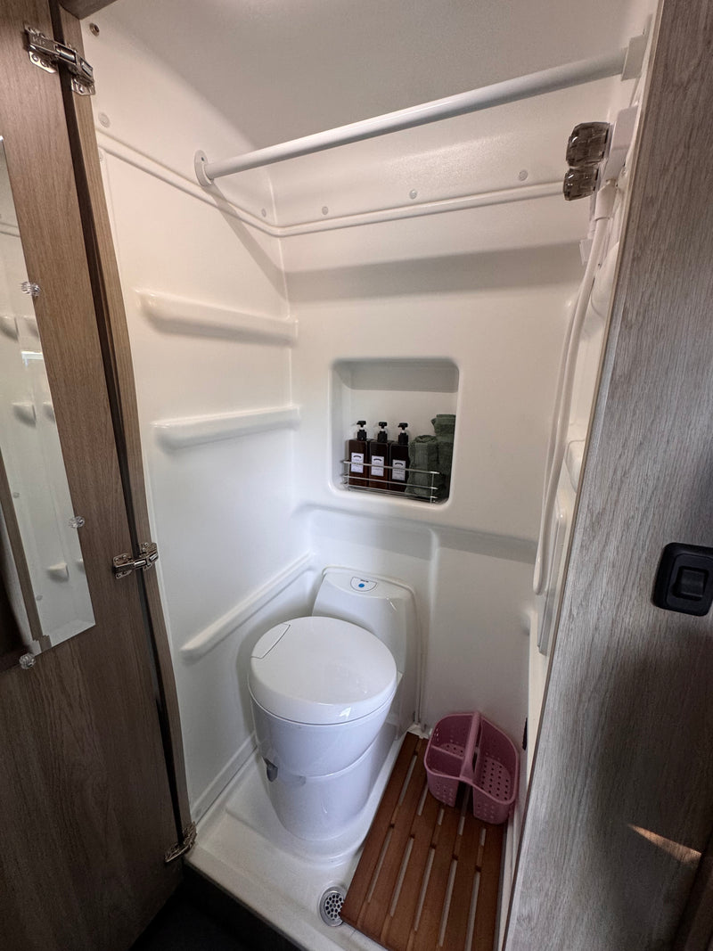 Compact RV rental wet bath with toilet, shower area, built-in shelf for toiletries, and wooden floor mat. — photo 15