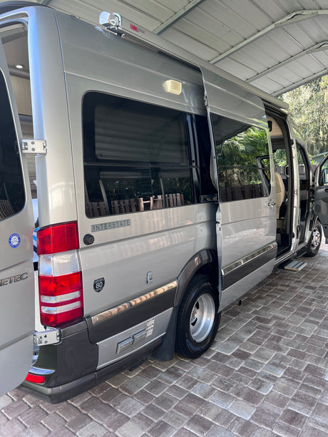 RV rental: Silver Airstream Interstate camper van on pavers with open side and rear doors, parked under a carport.