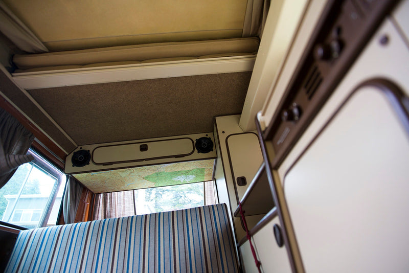 Cozy RV rental camper van interior featuring a raised pop-top bed, map headliner, striped bench, and storage. — photo 8