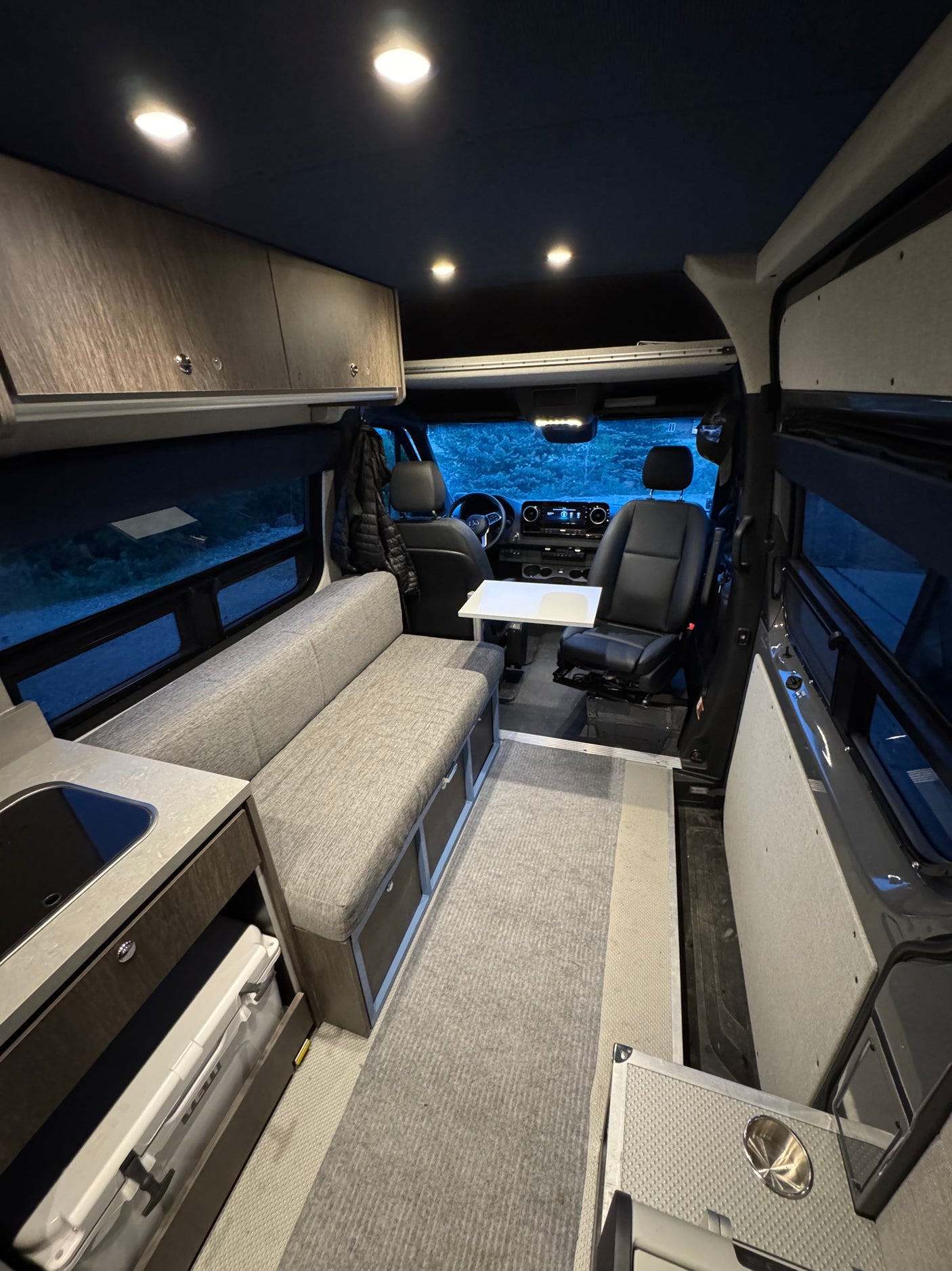 Modern RV rental interior: bright lights illuminate a functional kitchen, cozy seating, and driver's cabin. Ready for trips!
