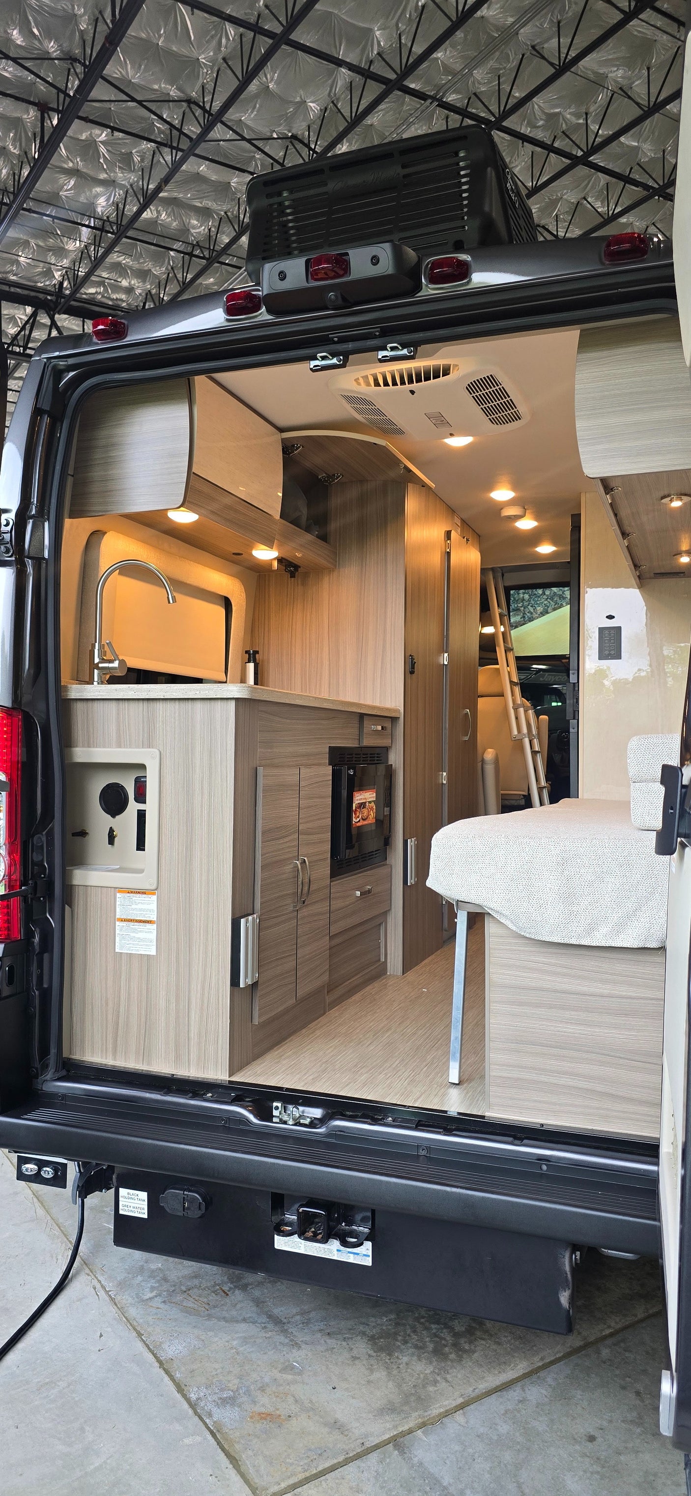 Spacious RV rental interior: kitchen, bed, and ladder visible from the rear of this modern camper van.