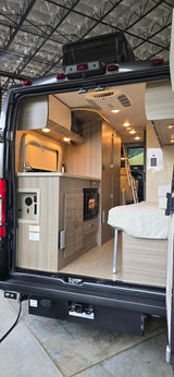 Spacious RV rental interior: kitchen, bed, and ladder visible from the rear of this modern camper van.