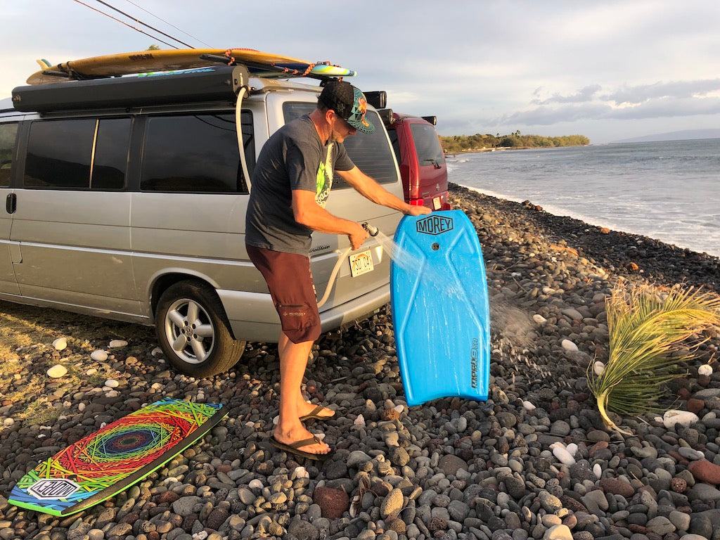 After a surf session, a man washes his bodyboard by his rv rental van on a rocky beach. Surfboards are on the roof. — photo 15