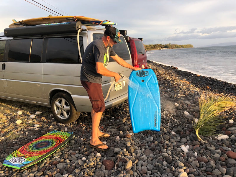 After a surf session, a man washes his bodyboard by his rv rental van on a rocky beach. Surfboards are on the roof. — photo 15