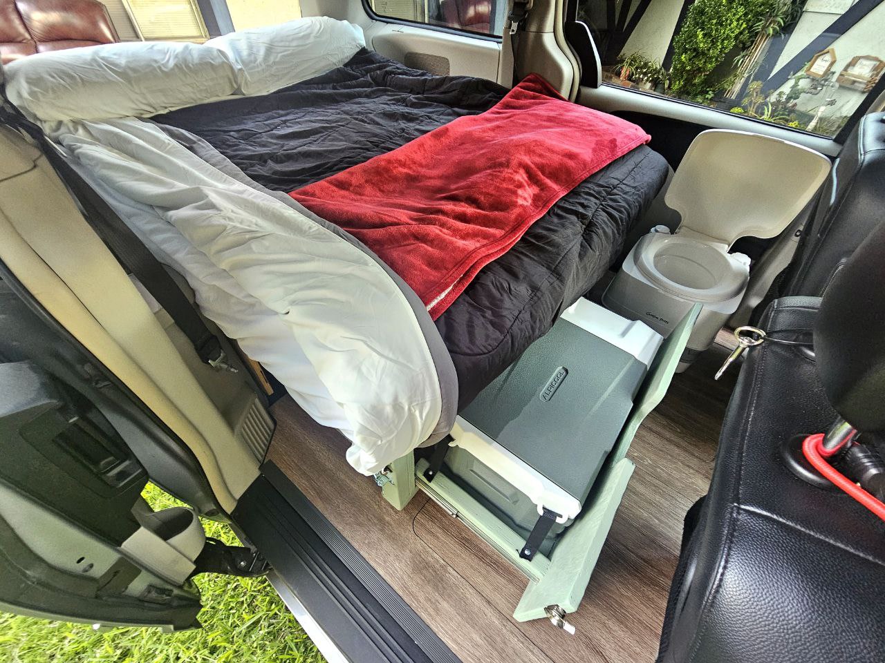Interior view of an RV rental van, showing a bed, portable toilet, and cooler for compact living & travel. — photo 11