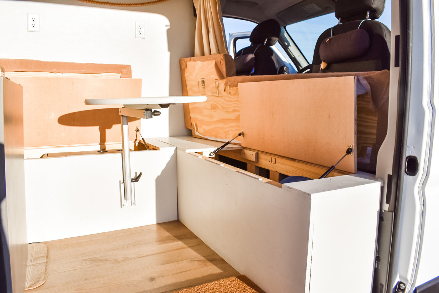RV rental interior: A bright camper van conversion with custom white storage benches, an adjustable table, and hidden compartments. — photo 9