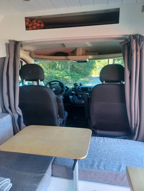 Cozy rv rental interior: view of driver's cab from living area with table, seats, and overhead storage. Perfect for road trips!