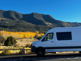 White RV rental van parked against a backdrop of mountains, vibrant yellow aspens, and a clear blue sky.