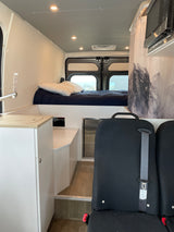 RV rental interior: cozy bed, sink, microwave, fridge, and passenger seating. Perfect for adventure travel.