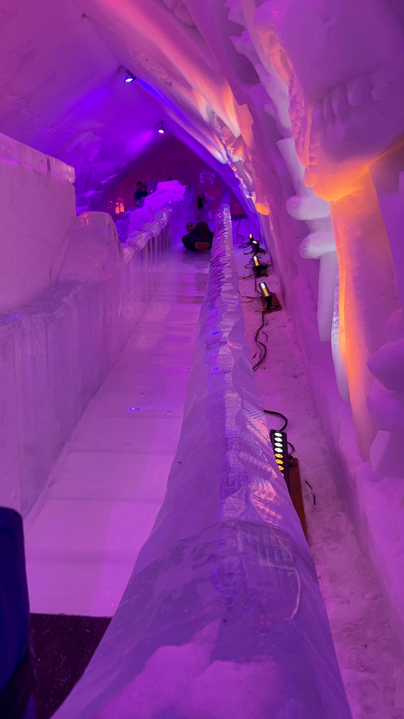 A glowing purple ice tunnel with an ice slide, lit by orange accents. A memorable destination for your RV rental trip!