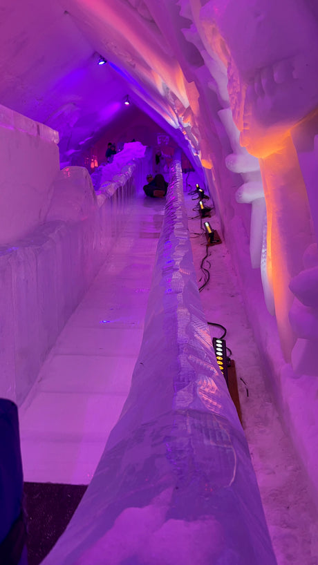 A glowing purple ice tunnel with an ice slide, lit by orange accents. A memorable destination for your RV rental trip!
