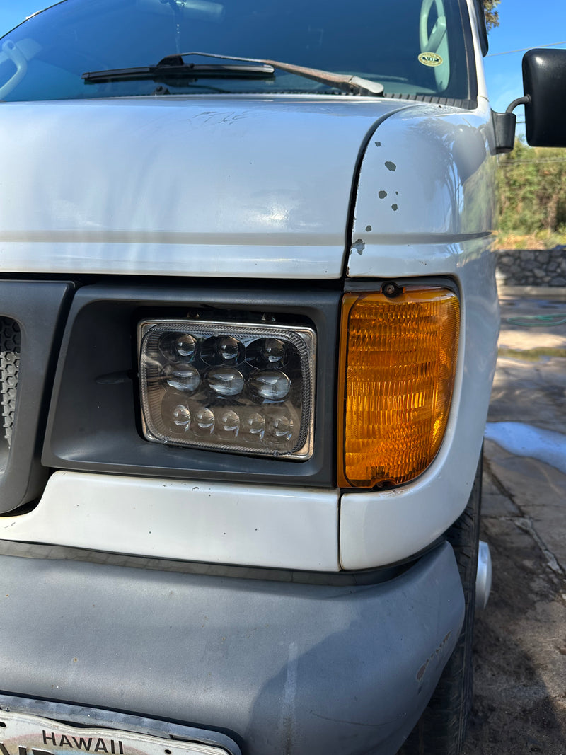 Front right of a white RV rental van, showing an LED headlight, amber turn signal, and paint wear. Hawaii plate. — photo 3