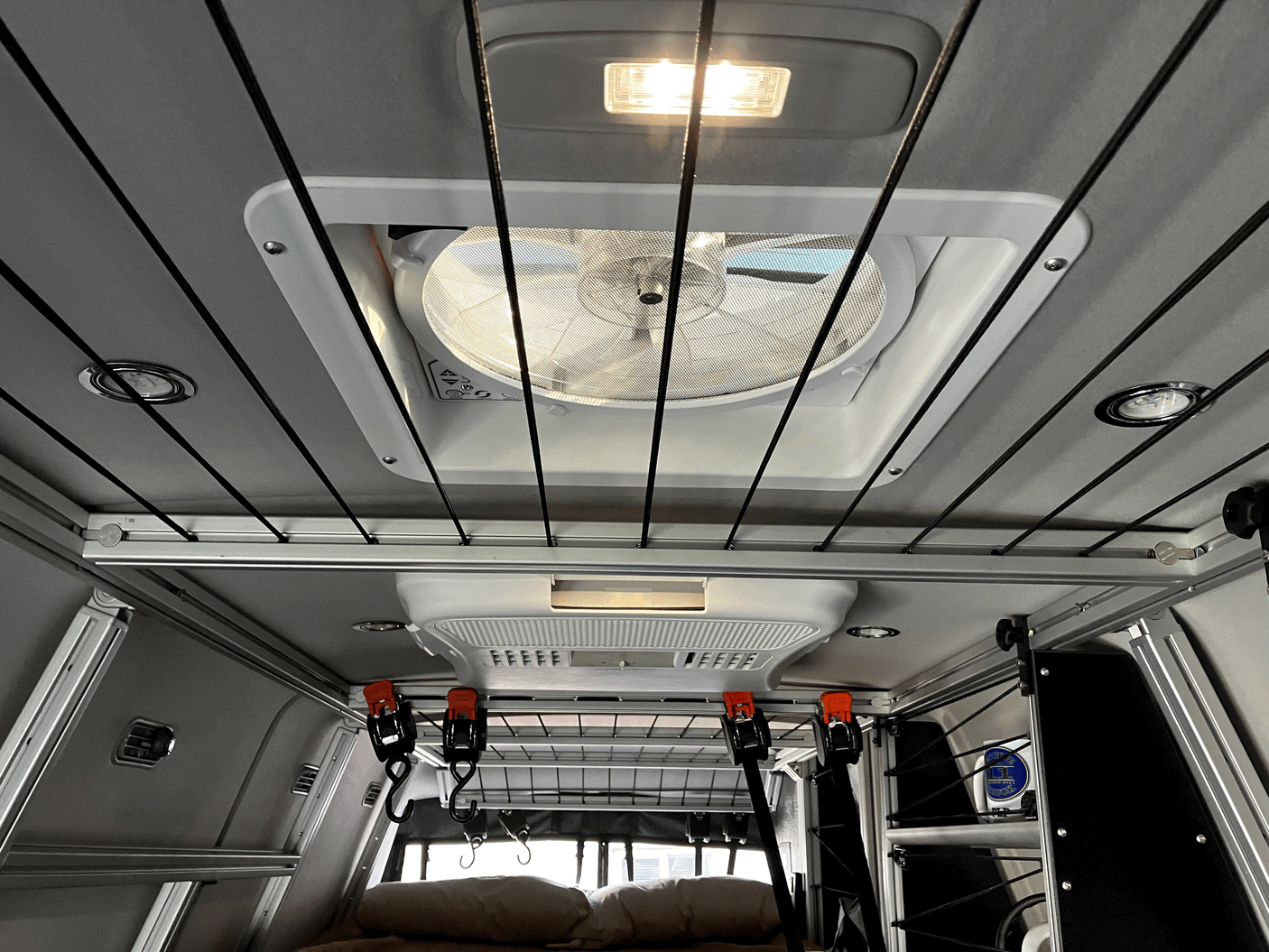 Inside an RV rental: a Maxxair fan, bright lights, and ceiling-mounted bungee cords for gear storage.