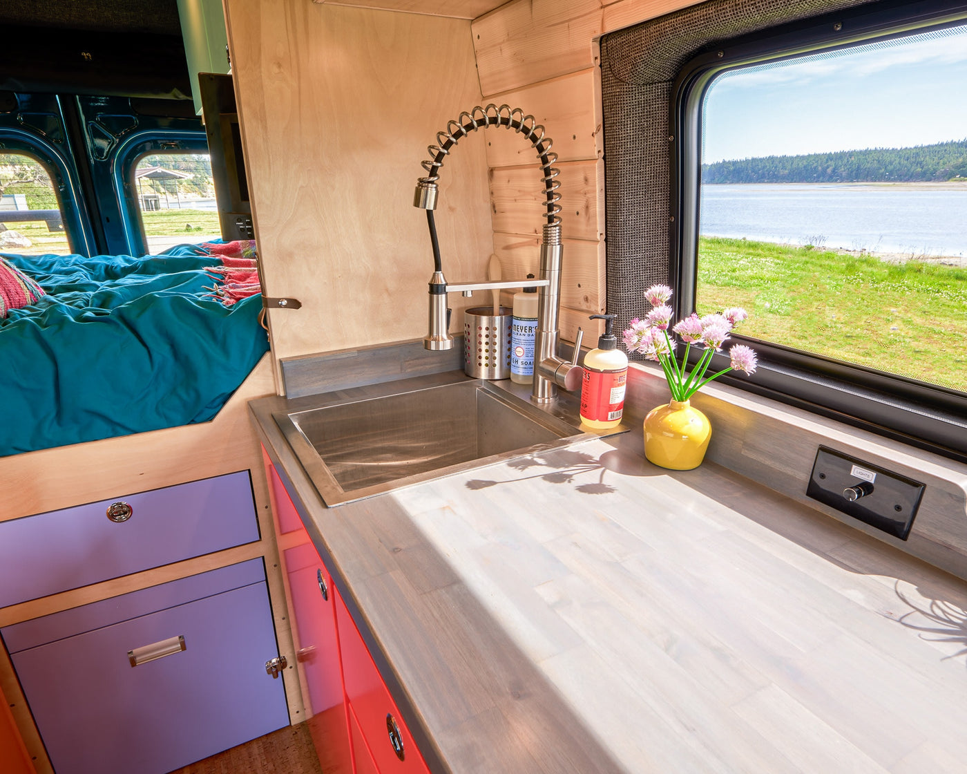 Cozy RV rental interior featuring a functional kitchen with sink, vibrant bed, and scenic window view for your adventure. — photo 8