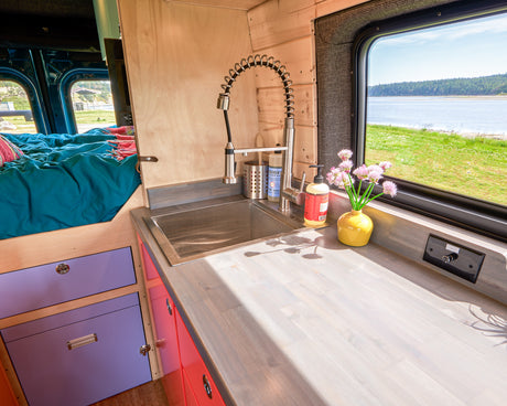 Cozy RV rental interior featuring a functional kitchen with sink, vibrant bed, and scenic window view for your adventure.