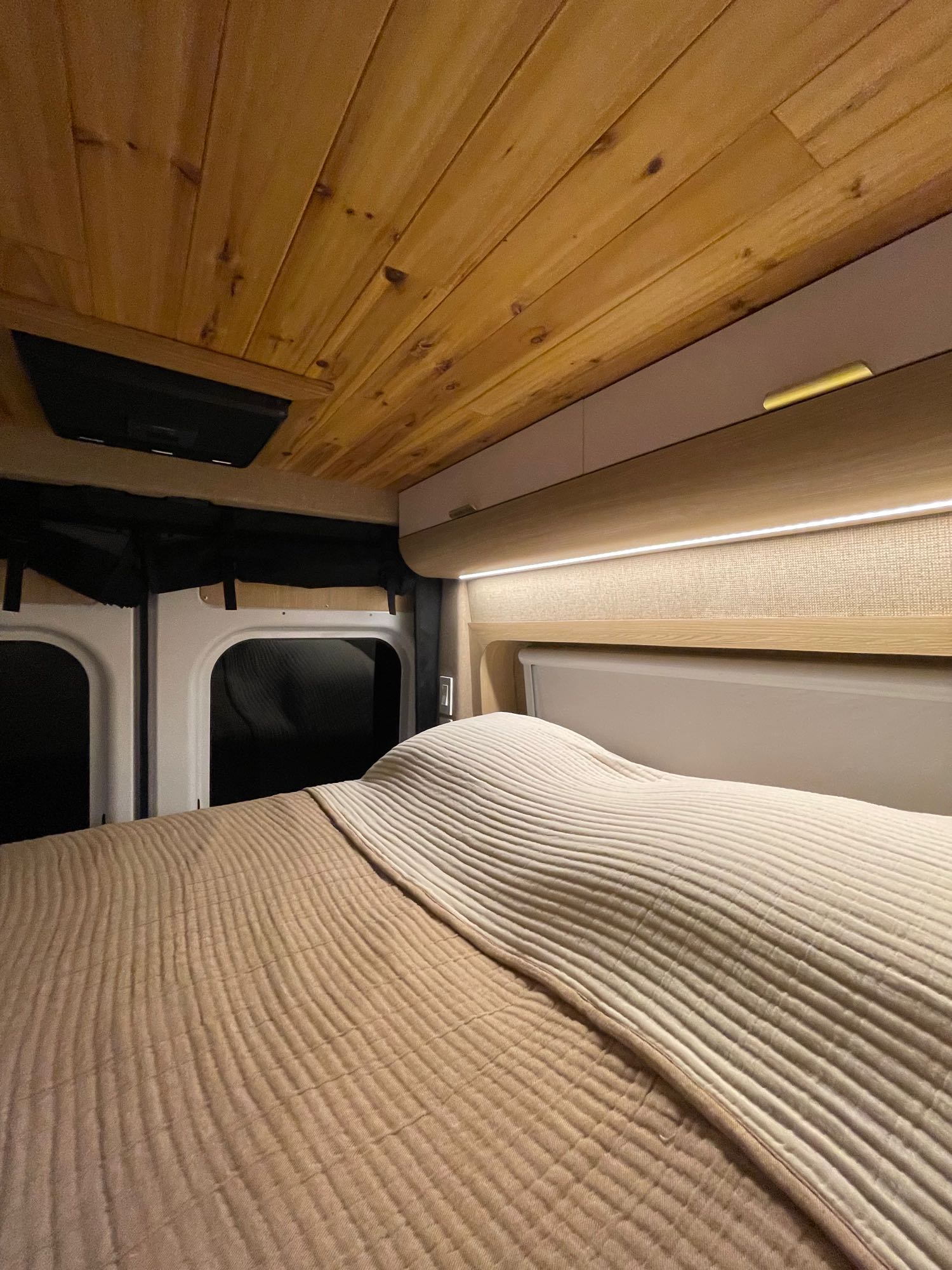 Experience comfort in this RV rental's cozy sleeping area, with a plush bed, wood ceiling, and ambient LED lighting.