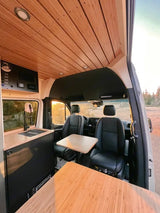 Cozy rv rental van interior with wooden ceiling, kitchen, swiveling seats, and dining tables, perfect for travel.