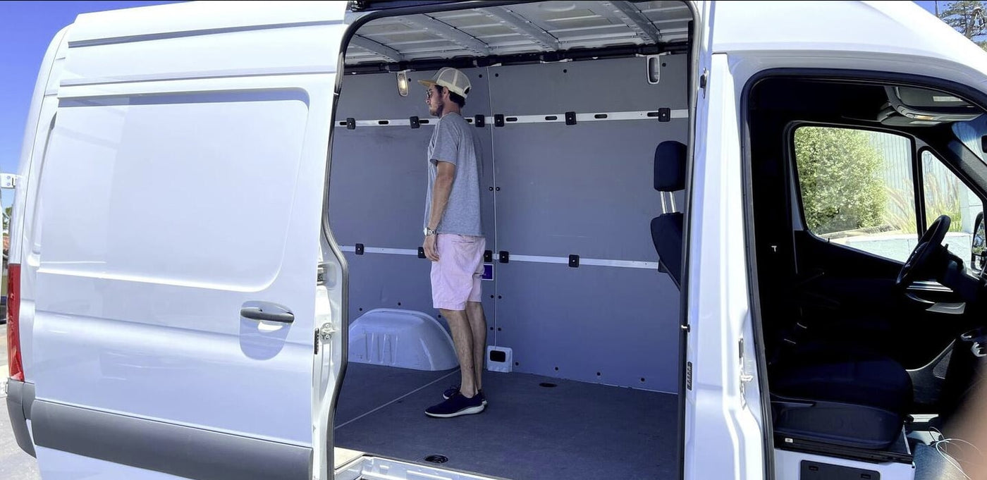 Man standing inside a spacious white cargo van, demonstrating its interior for potential RV rental or custom conversion. — photo 10