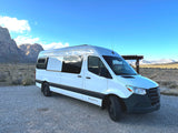 This white VANSMIth RV rental van is parked in a vast desert with rugged mountains, ready for adventure.