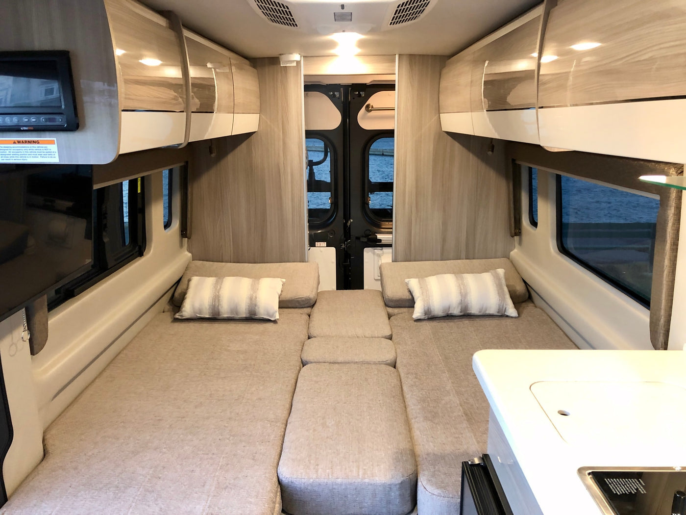 Bright RV rental interior features two convertible beds forming a large sleeping area, overhead storage, and a compact kitchen counter. — photo 10