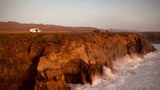 RV rental van on a dramatic coastal cliff. Waves crash below, offering stunning views and remote adventure.