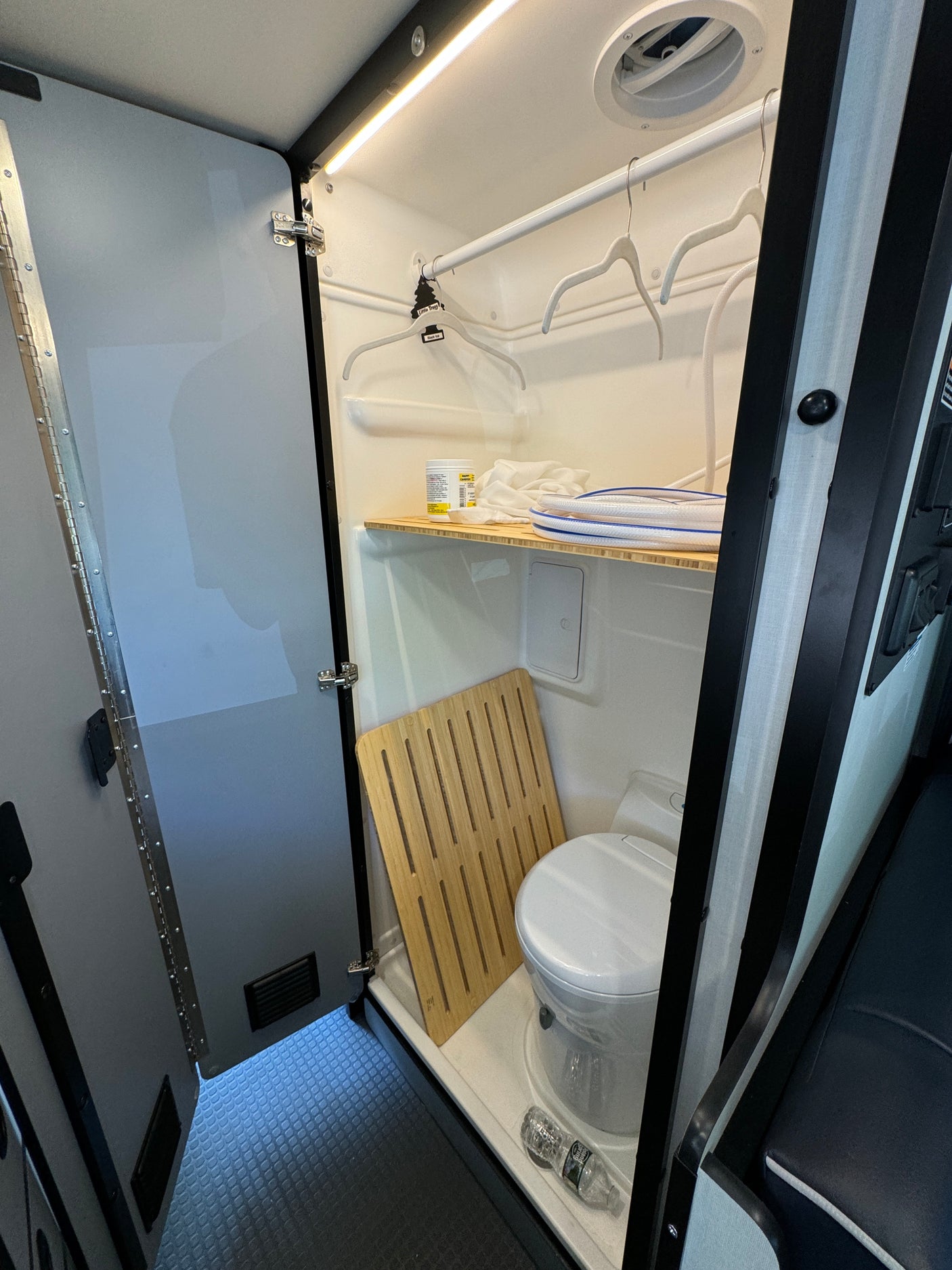 Step inside this compact RV rental wet bath, featuring a toilet, shower mat, storage shelf, and hanging rod.