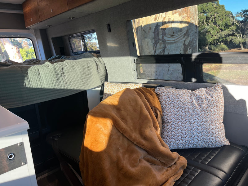 Cozy RV rental interior with a bed, plush seating, and bright views of outdoor trees under sunlight. — photo 15