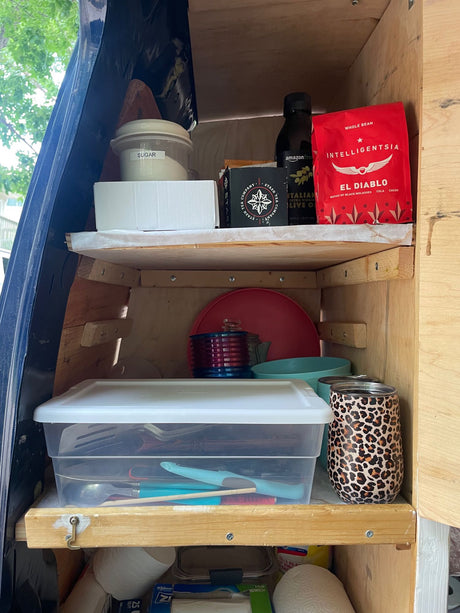 This RV rental features organized kitchen storage with shelves holding coffee, olive oil, sugar, plates, and utensils for compact travel.