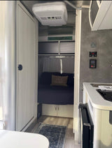 Compact RV rental interior featuring a bed, kitchenette, and control panels, offering cozy travel convenience.