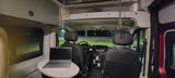 Inside an RV rental at night: a well-lit mobile office space with a laptop on a table, facing the driver's cabin.