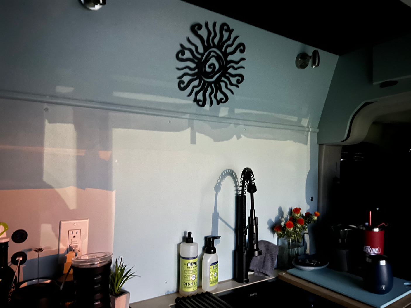 Stylish RV rental galley showcasing a functional sink, coffee corner, and decorative sun wall art.