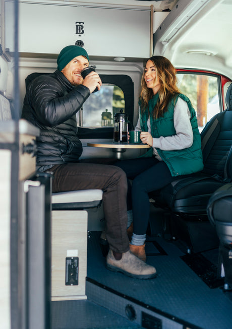 A joyful couple enjoys coffee inside their modern RV rental, perfect for cozy road trips and camping adventures.