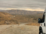 RV rental exploring a vast desert landscape with mountains and a winding dirt road under cloudy skies. Great for adventure travel.