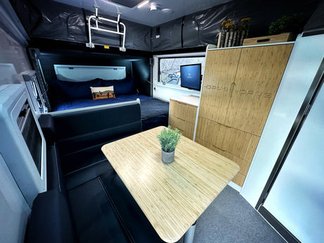 Cozy RV rental interior featuring a modern pop-up camper design with a bed, TV, wood cabinets, and dining table.