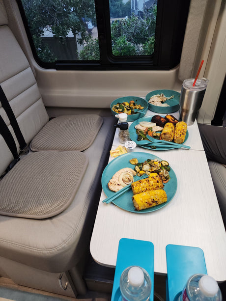 Mealtime in an RV rental: grilled corn, chicken, and roasted veggies on blue plates. A cozy dining setup perfect for road trips.