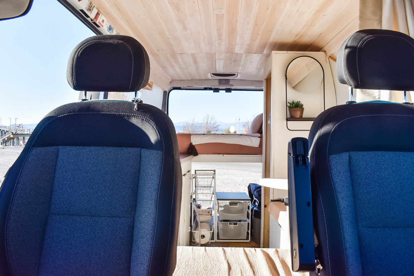 Spacious RV rental interior with front seats, wooden ceiling, cozy bed, and smart storage solutions for travel.