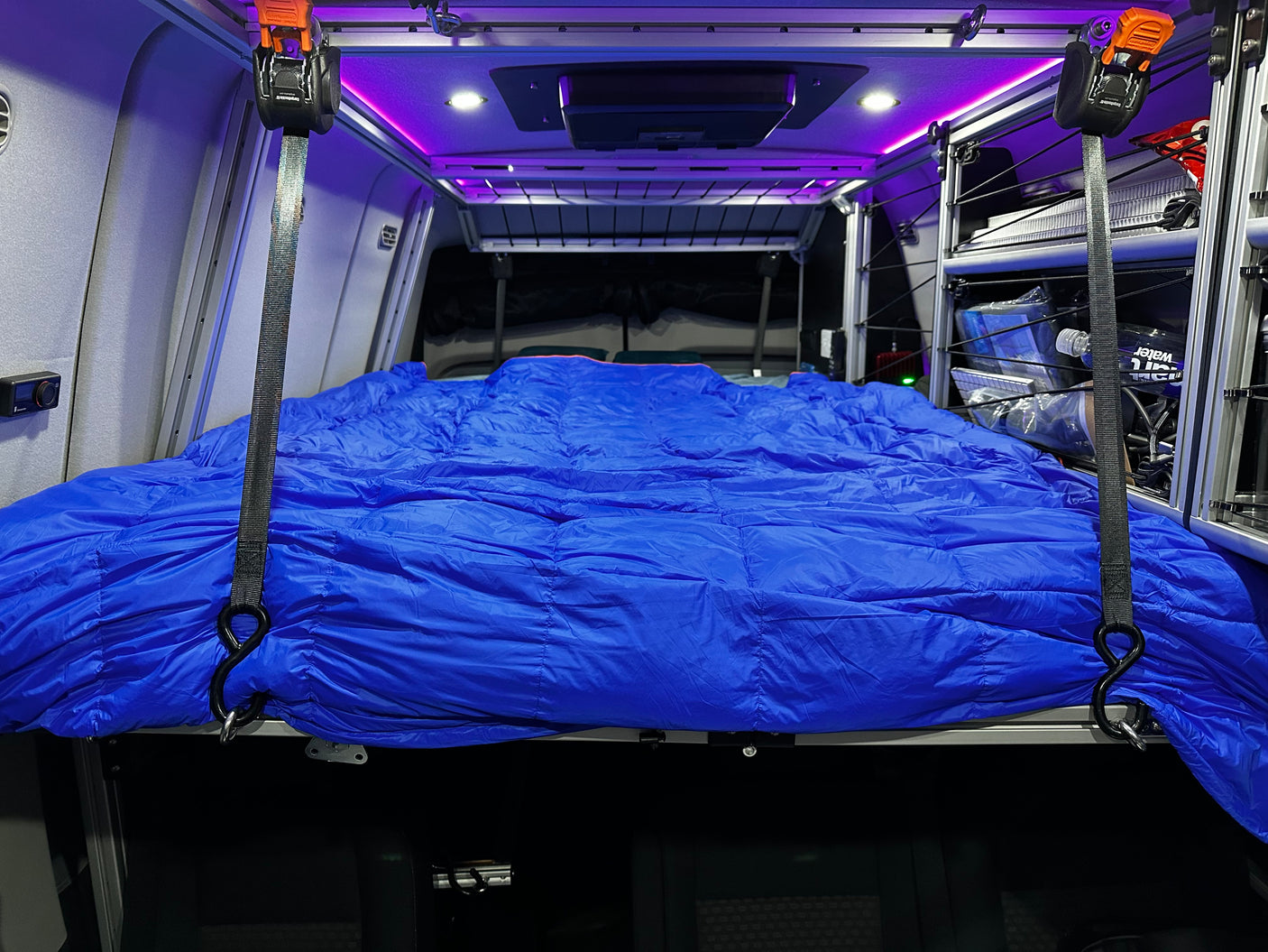 This RV rental interior offers a comfortable blue sleeping setup on a raised platform, with ambient lighting and organized storage.