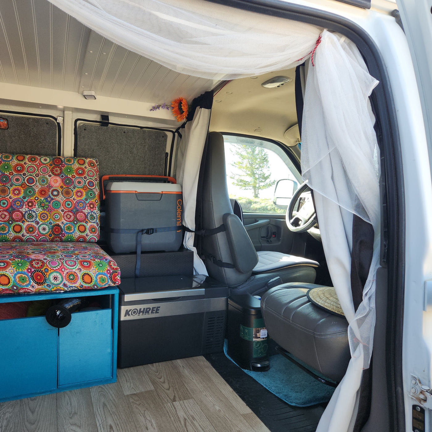 Inside a custom RV rental, a cozy van conversion with colorful cushions, compact fridge, and storage, ready for adventure. — photo 15