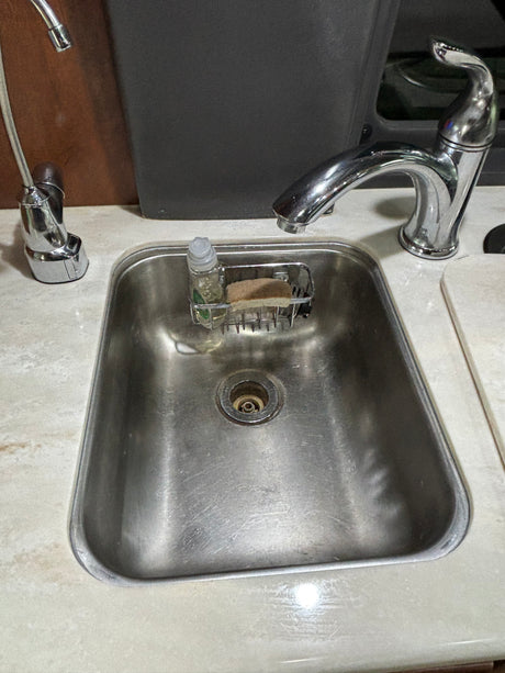 Compact stainless steel sink, faucets, soap dispenser, and sponge in an RV rental kitchen area.
