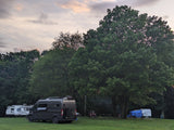 A dark camper van and two travel trailers at a green campsite with trees under a cloudy sky, showcasing diverse RV rental options.