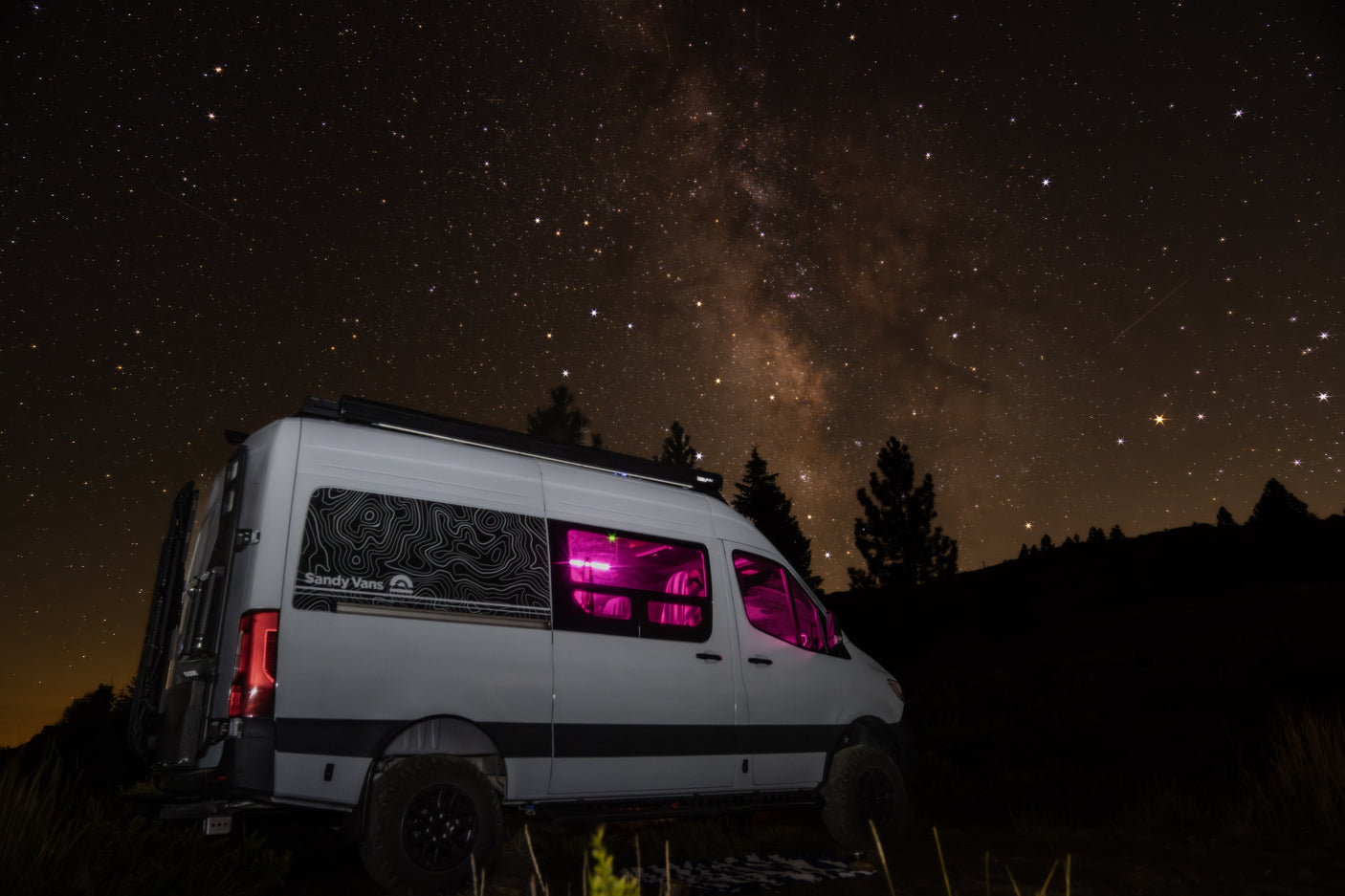 Stunning Milky Way views above an RV rental camper van with vibrant pink interior lights, perfect for a starry night adventure.