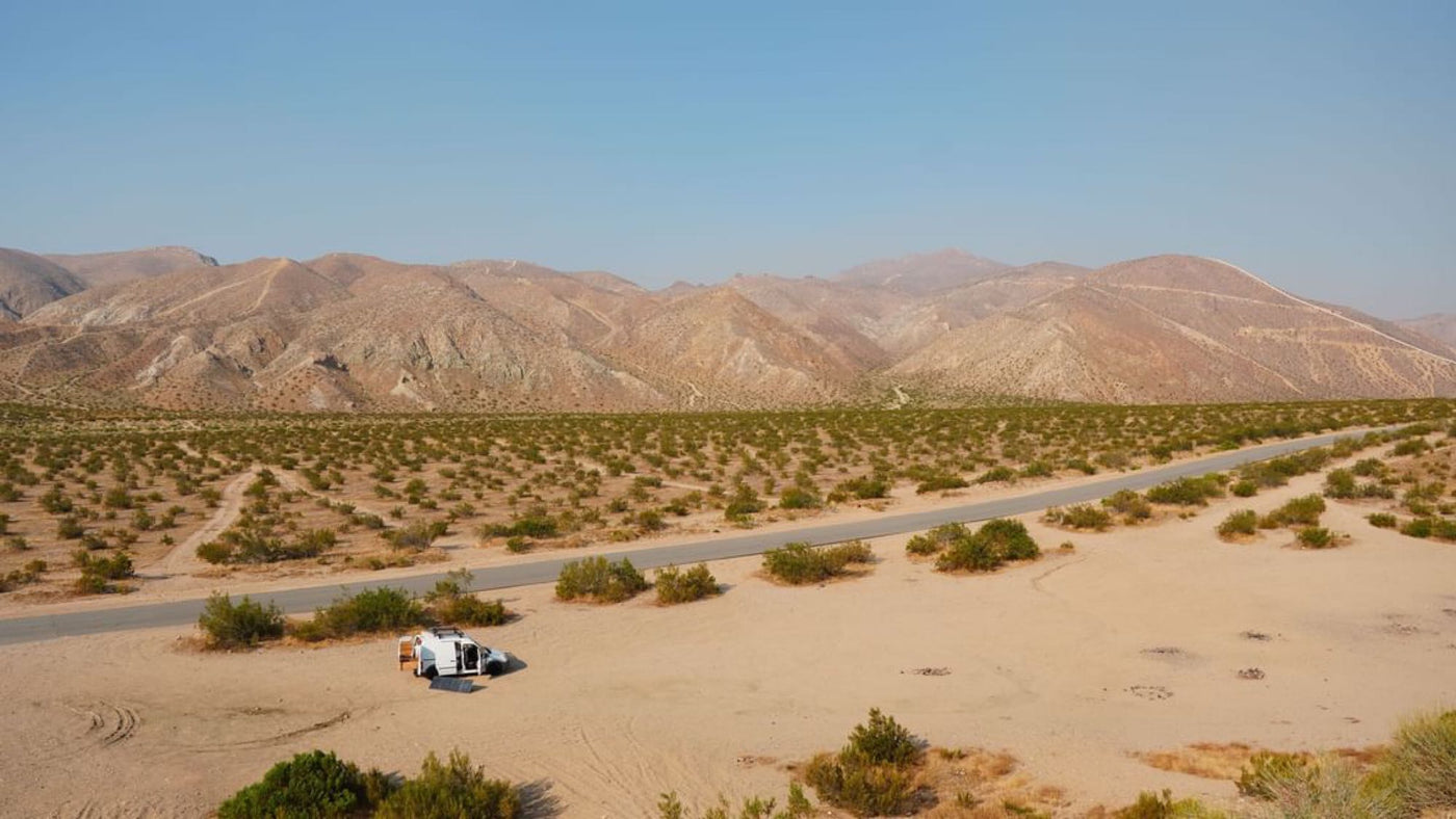 White RV rental parked with door open and solar panel in vast desert landscape with distant mountains. — photo 5