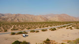 White RV rental parked with door open and solar panel in vast desert landscape with distant mountains.