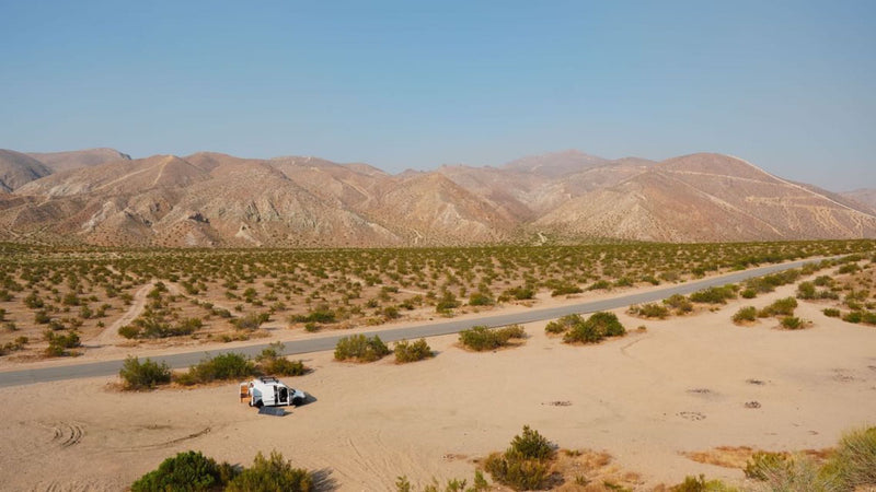White RV rental parked with door open and solar panel in vast desert landscape with distant mountains. — photo 5