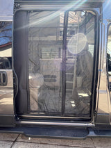 Grey RV rental van's open side door reveals a black mesh screen and the interior: a kitchen area & ladder.