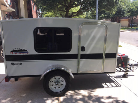 White, compact 'Runaway Navigator' RV rental, perfect for travel. Features a window, door, and chrome fender.