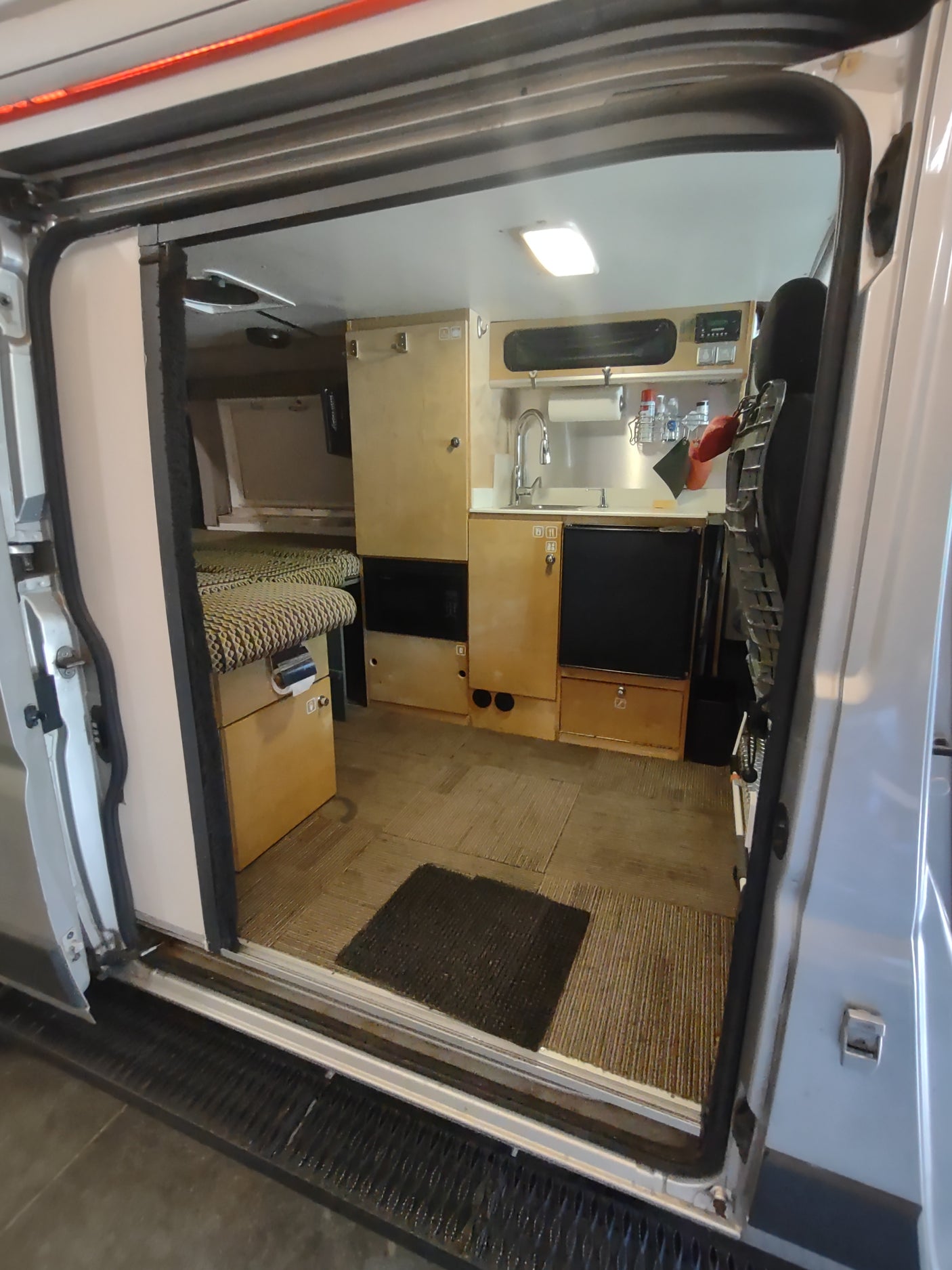 Interior view of an RV rental camper van, showing a compact kitchen with sink and storage, plus a living/sleeping area.