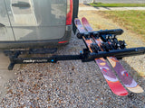 Grey rv rental van with a RockyMounts hitch-mounted ski rack displaying two pairs of skis, one with 'Argent The Badger' graphics.